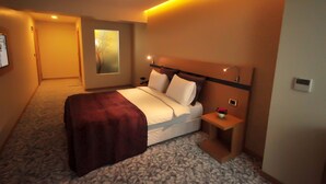 Quarto de hotel com uma cama, mesa de cabeceira, luminária na parede e um quadro.