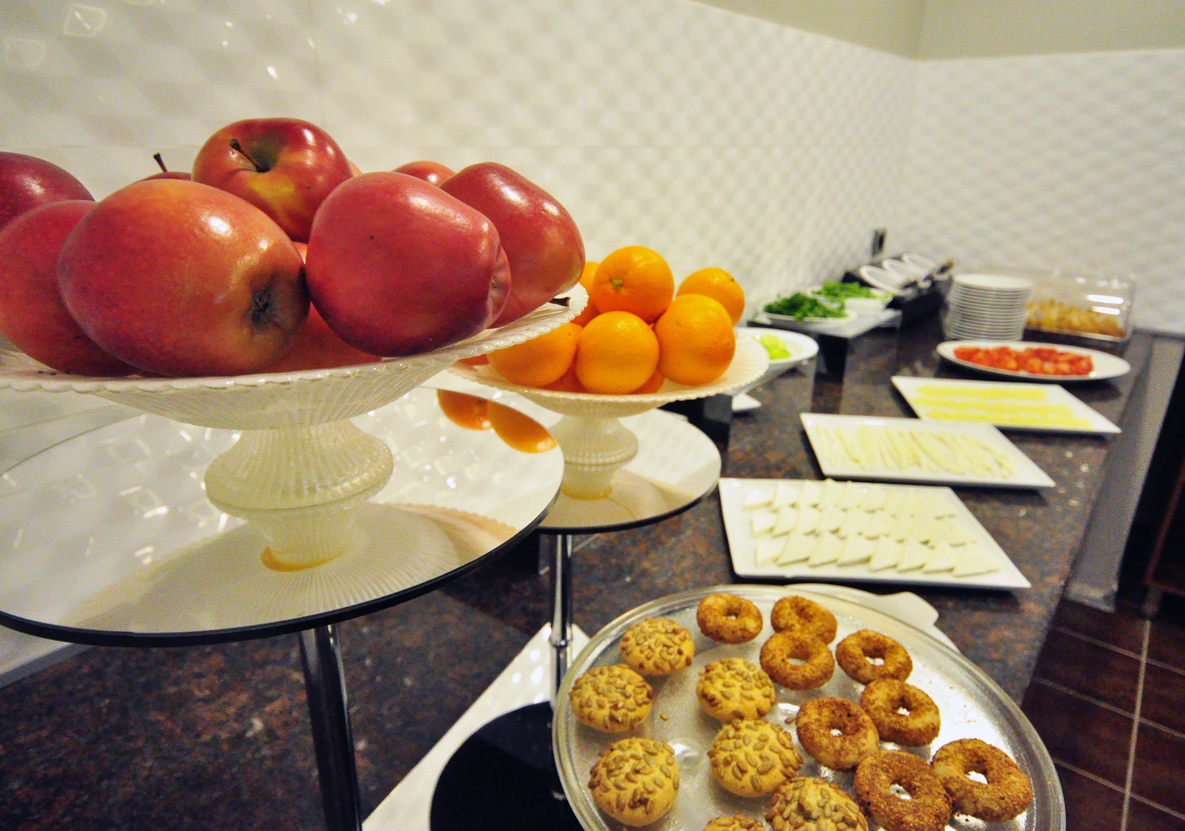A buffet table with various food items including apples, oranges, and pastries.