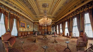 Uma sala imponente com lustres elaborados, carpetes estampados e móveis clássicos.