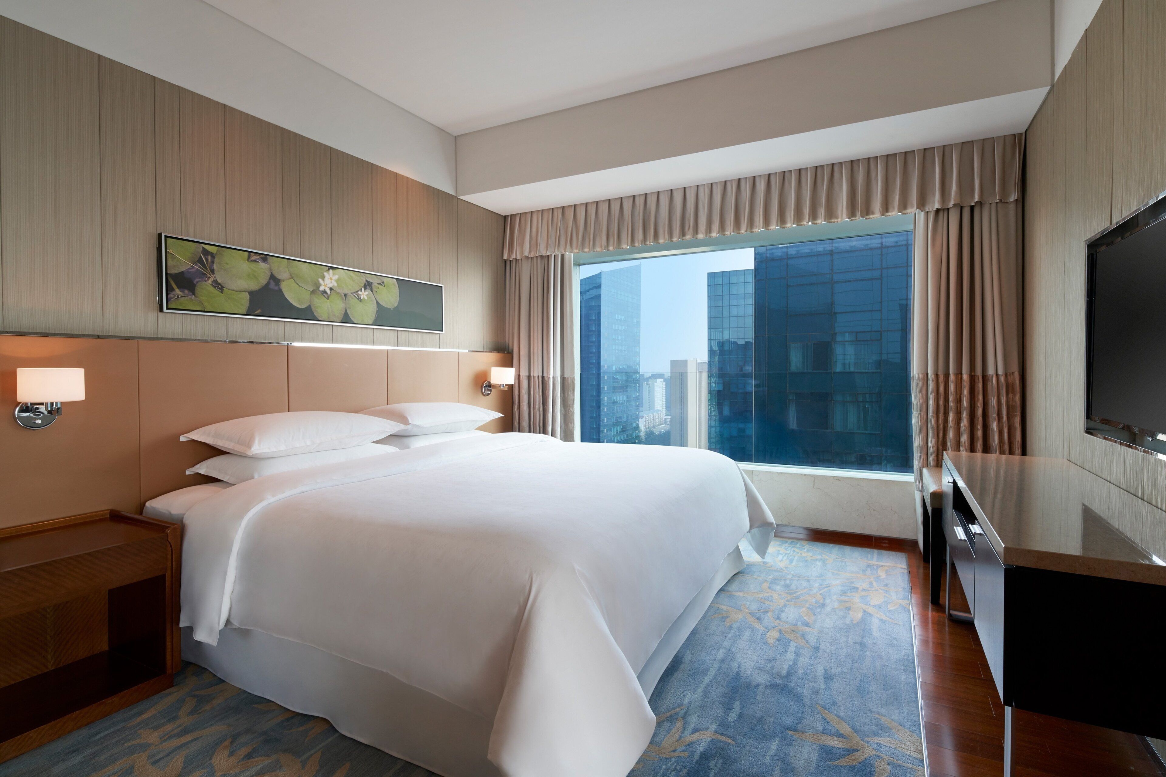 A hotel room with a large bed, a desk, a TV, and a city view.