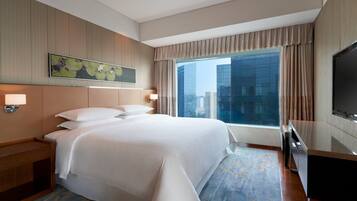 A hotel room with a large bed, a desk, a TV, and a city view.