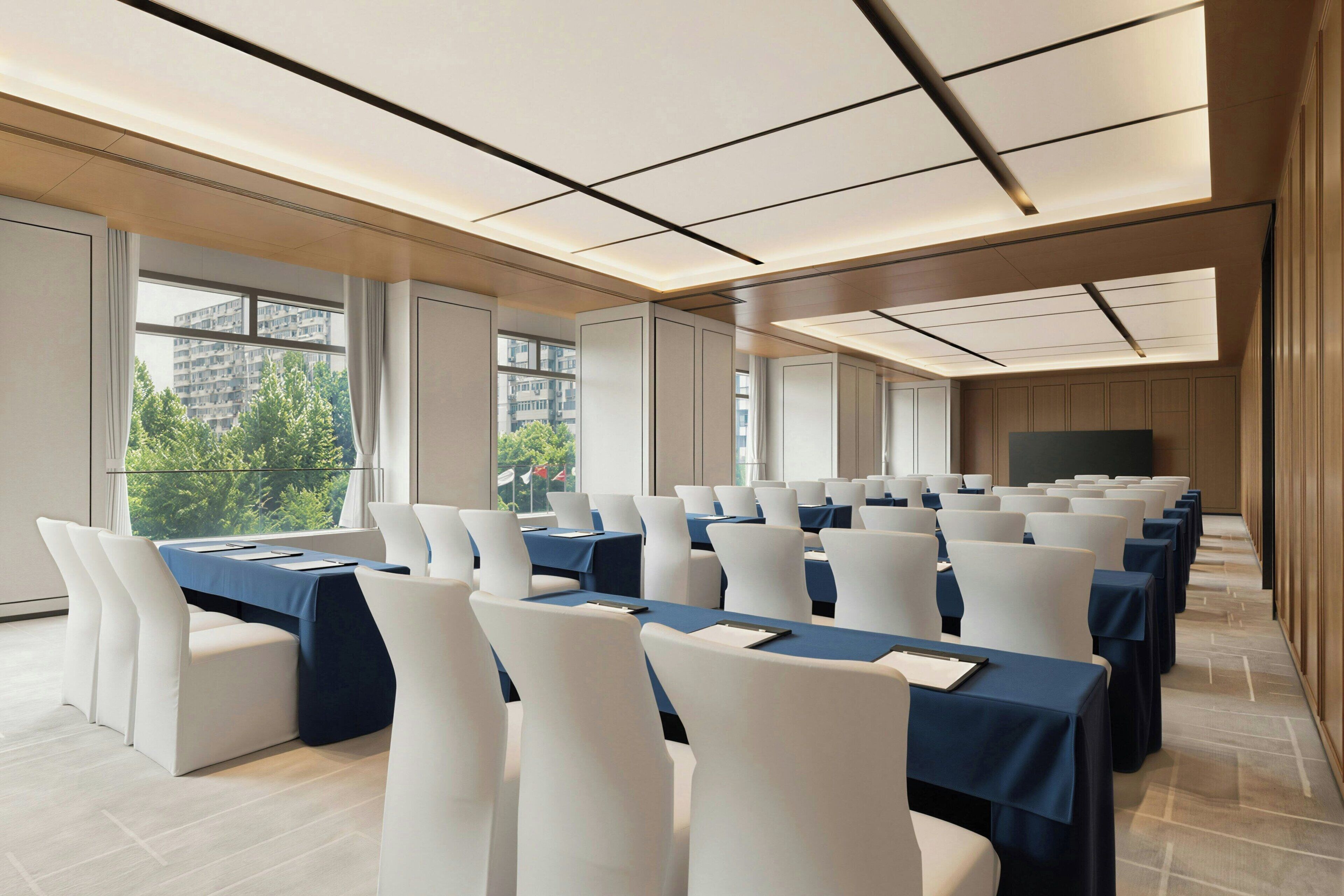 A conference room with rows of tables and chairs, large windows, and a flat-screen TV.