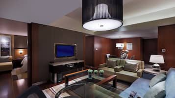 Una habitación de hotel moderna con televisor de pantalla plana, sofás de cuero, una mesa de centro de vidrio y una lámpara colgante grande.