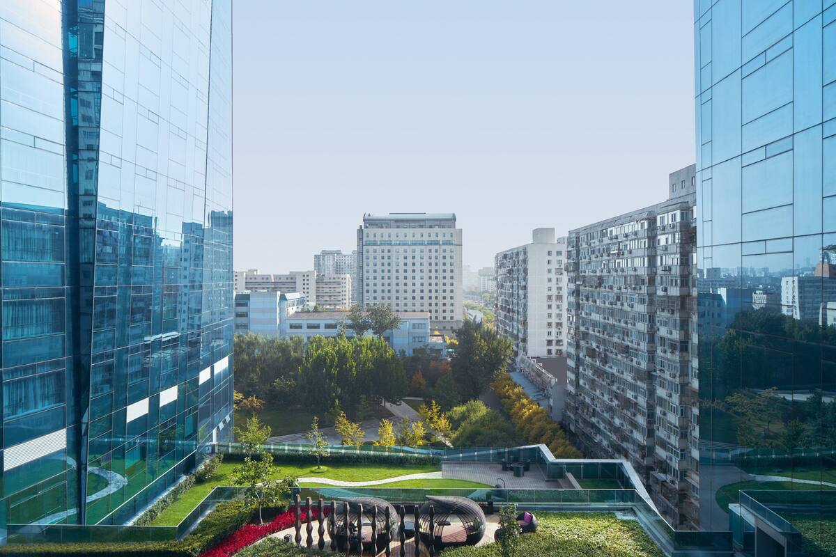 A modern urban landscape with high-rise buildings, a central park area with pathways, and a distinctive curved structure.