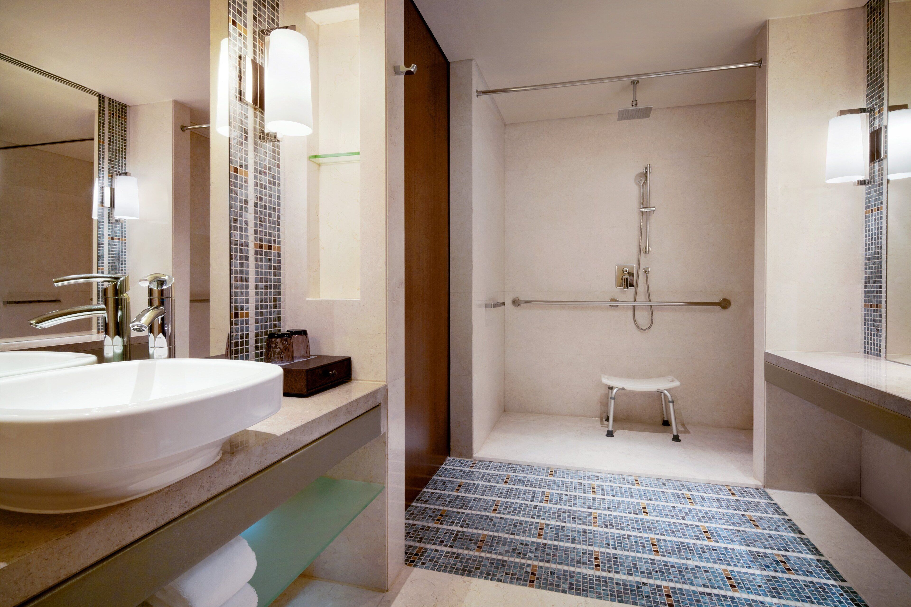 A modern bathroom with a large sink, a shower with a glass door, and a small stool.