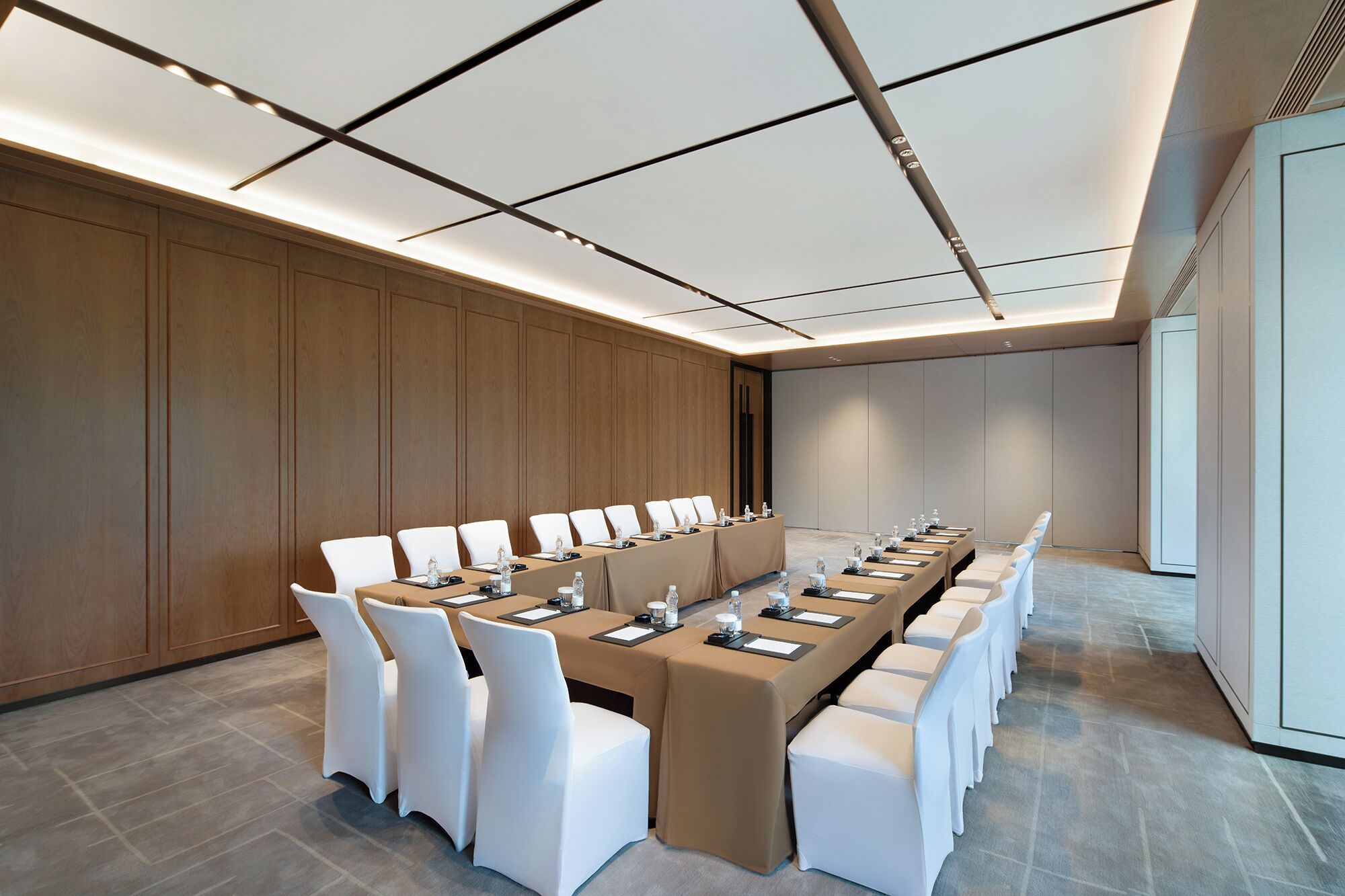 Un salón de conferencias con una larga mesa, sillas blancas y un panel de pared de madera.