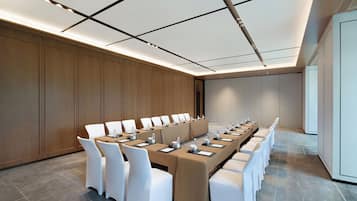 Konferenssihuone, jossa on pitkä pöytä, valkoiset tuolit ja puupanelilla verhoiltu seinä.