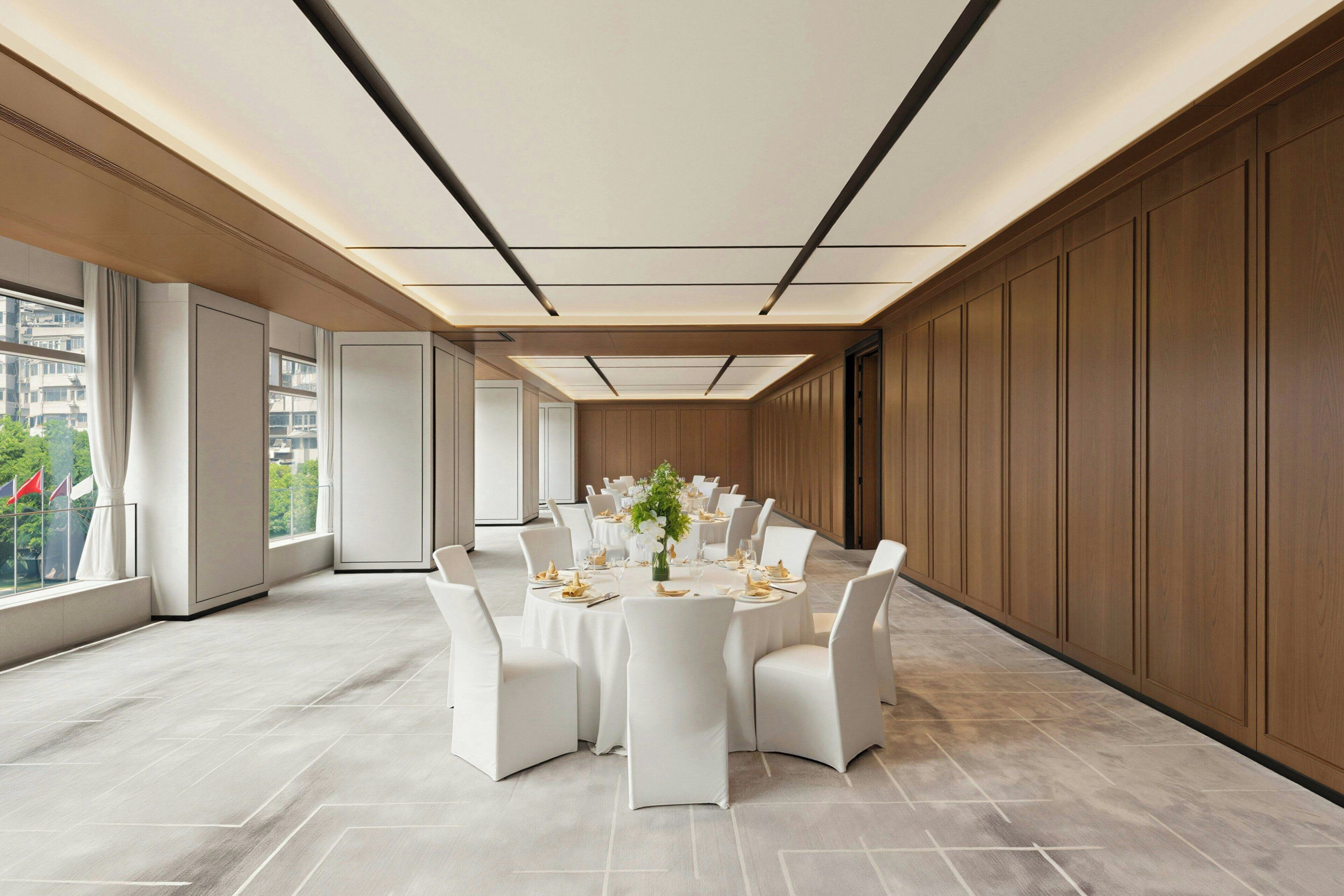 A conference room with a round table, white chairs, and a view of the city through large windows.