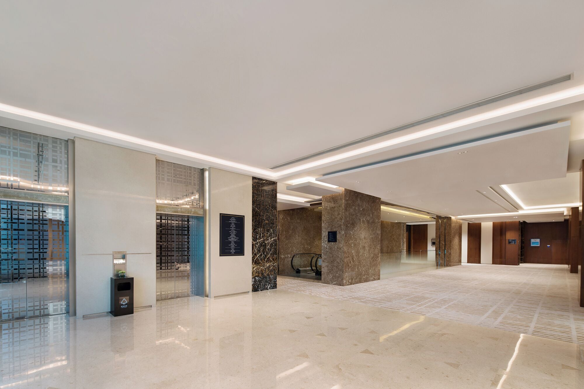 A modern hotel lobby with a marble floor, glass partitions, and a reception desk.
