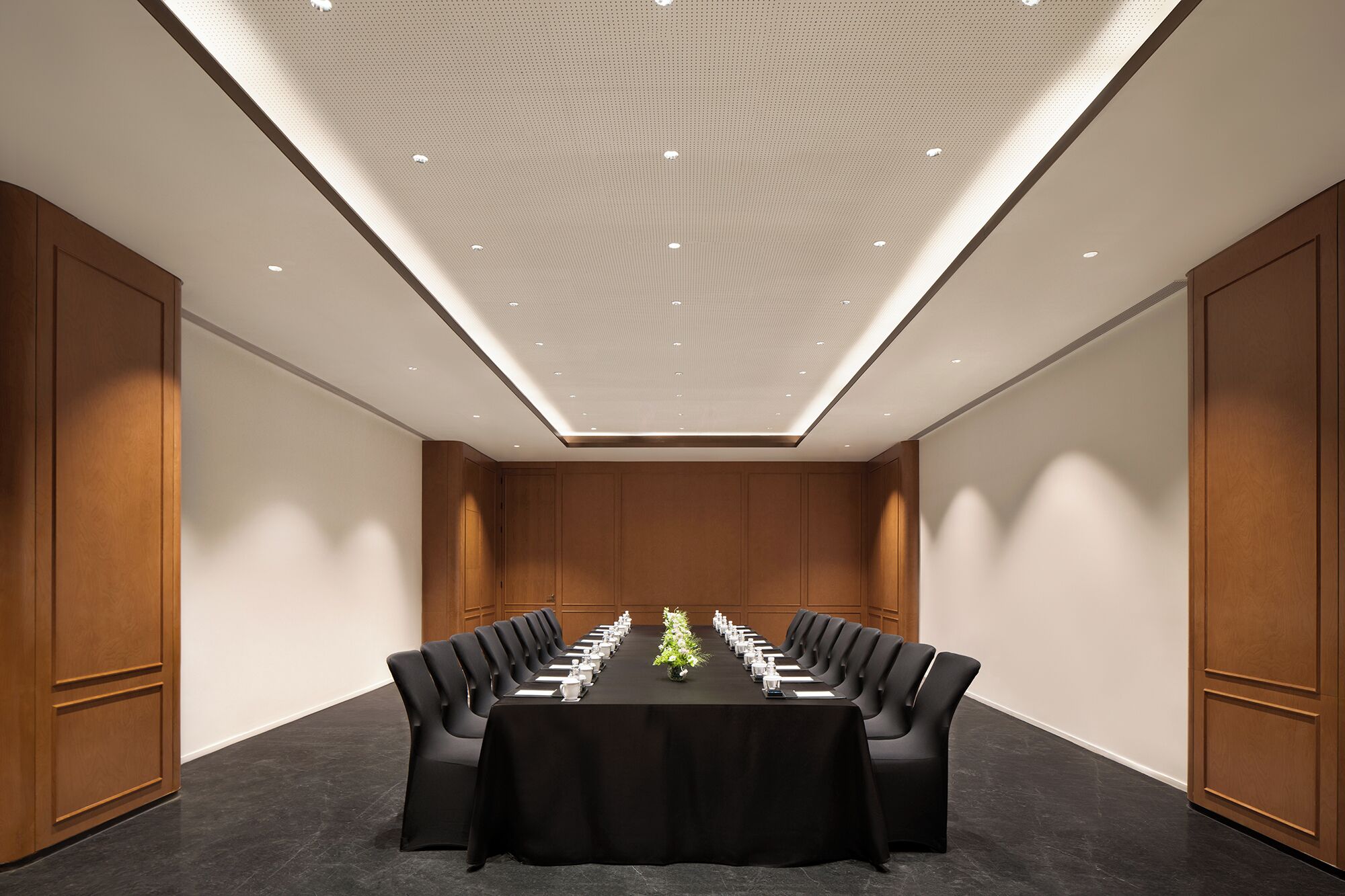 A conference room with a long table, black chairs, and a ceiling with recessed lighting.
