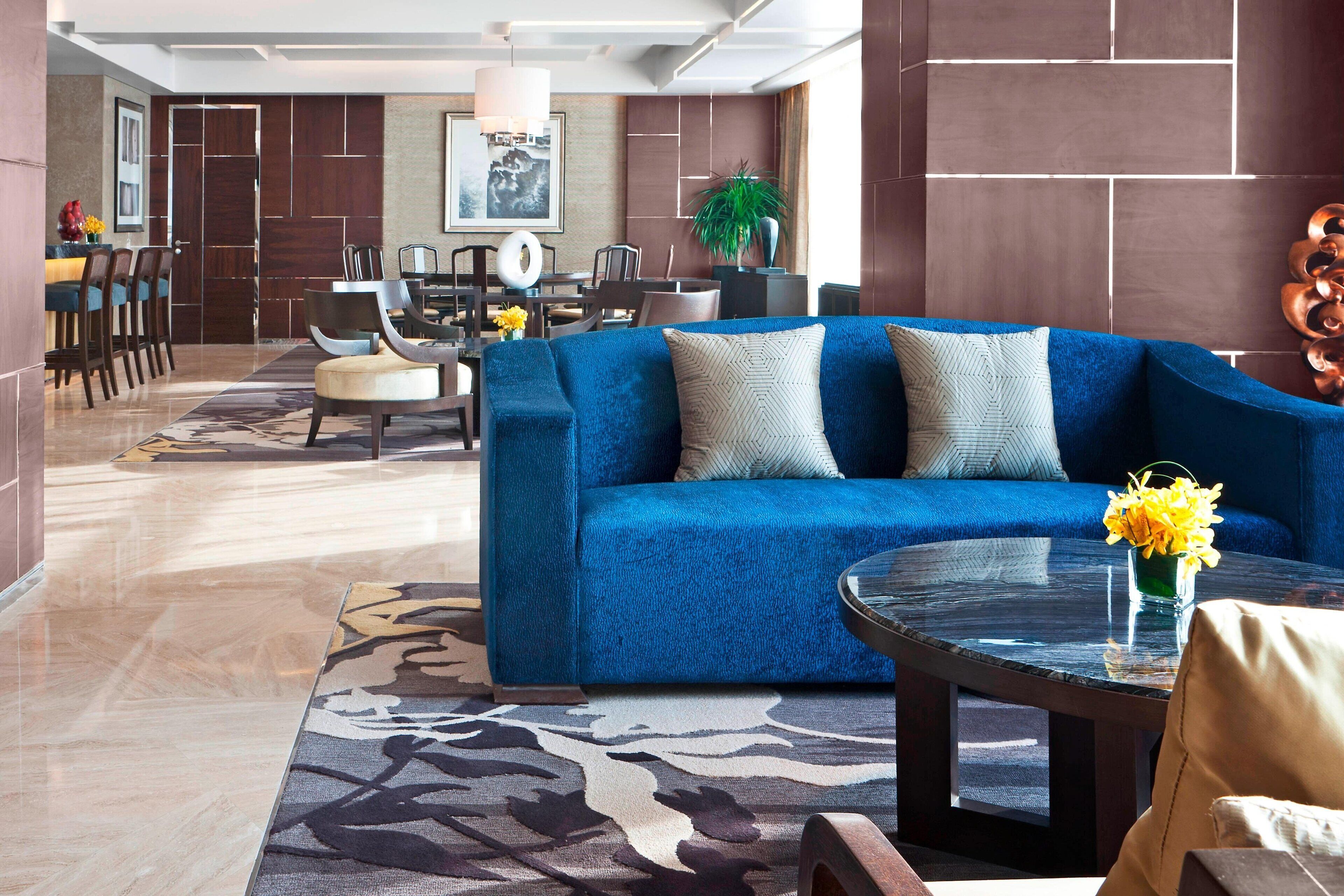 A modern living room with a blue sofa, a round coffee table, and a dining area in the background.