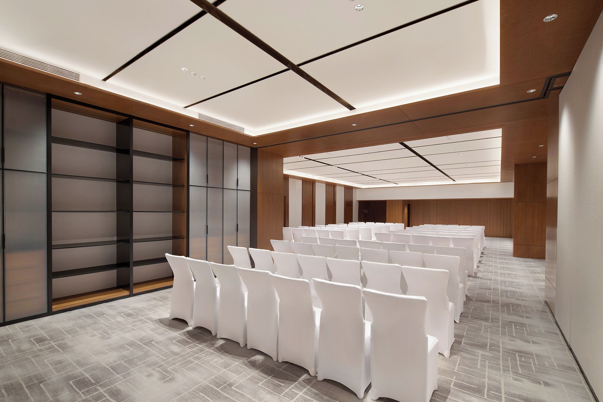 A conference room with rows of white chairs, a wooden panel wall, and a patterned floor.