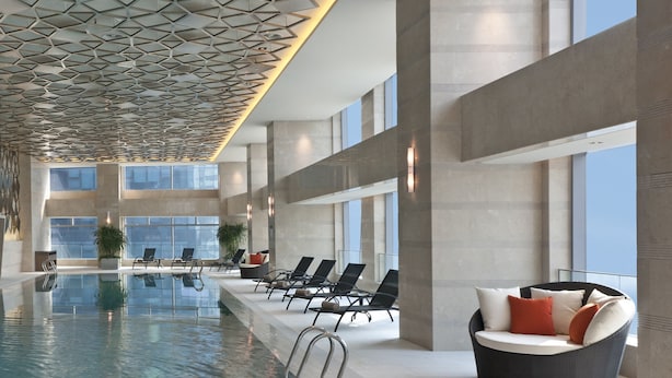 A modern indoor swimming pool with geometric ceiling design, lounge chairs, and large windows. - Sheraton Grand Beijing Dongcheng Hotel (Beijing)