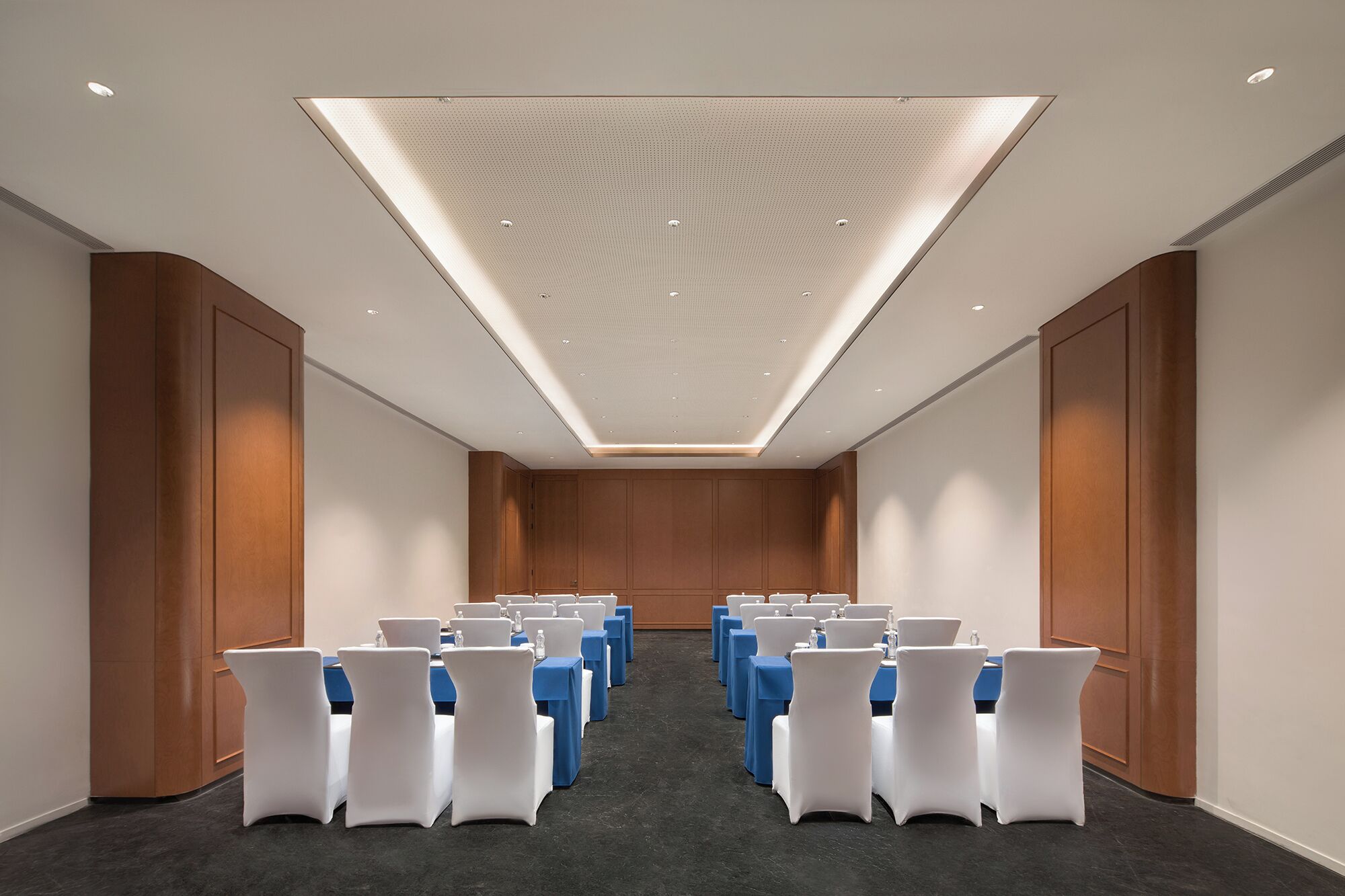 Une salle de conférence avec des rangées de tables et de chaises, un plafond à motifs et des lambris en bois sur les murs.