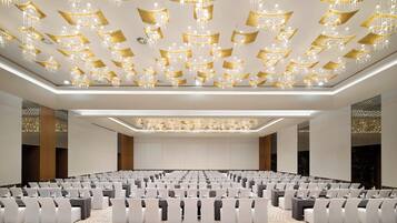 Une salle de conférence avec des rangées de tables et de chaises, une moquette à motifs et un plafond orné de lustres suspendus.
