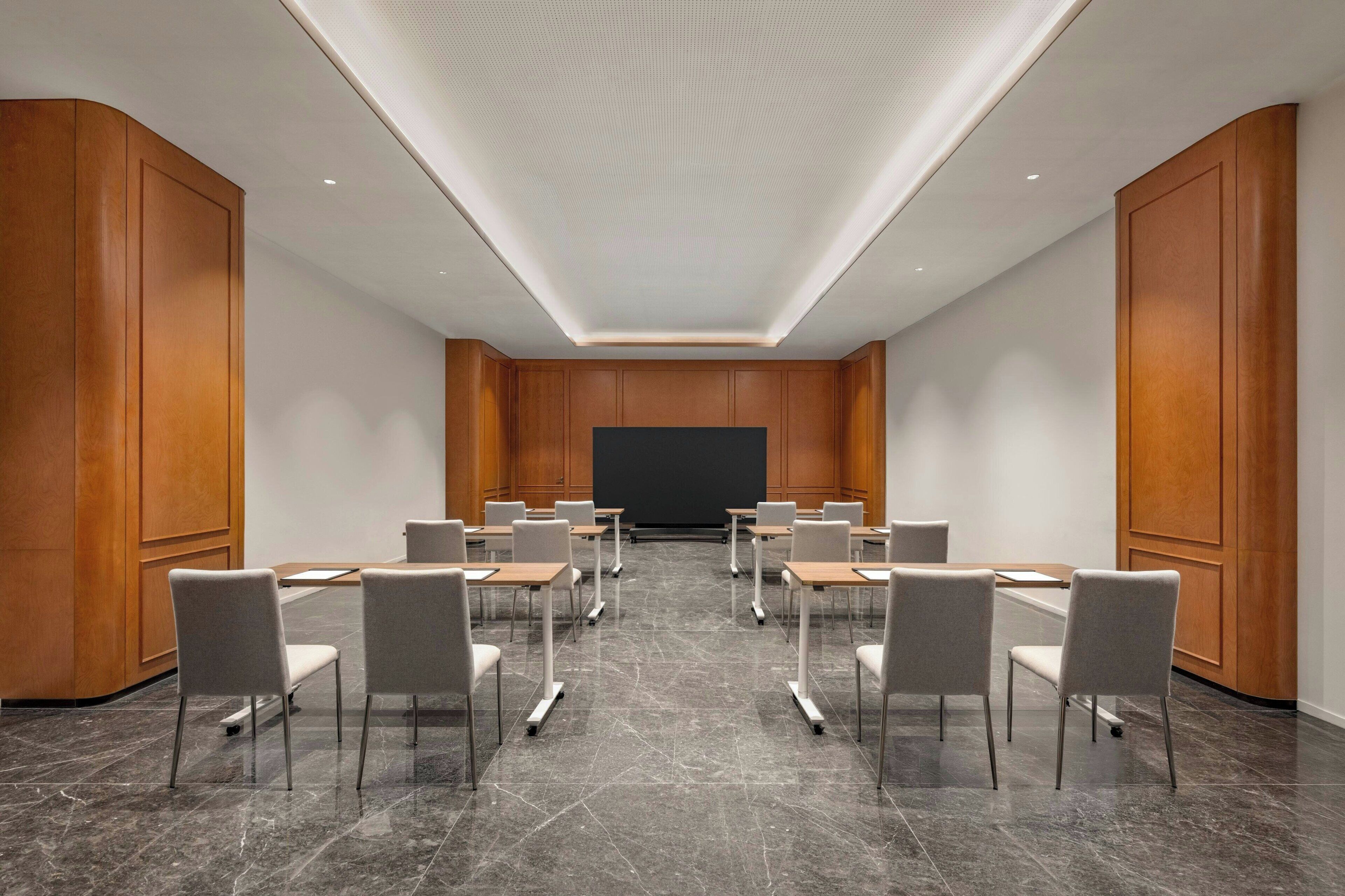 A conference room with a large screen, multiple tables, and chairs arranged for meetings.