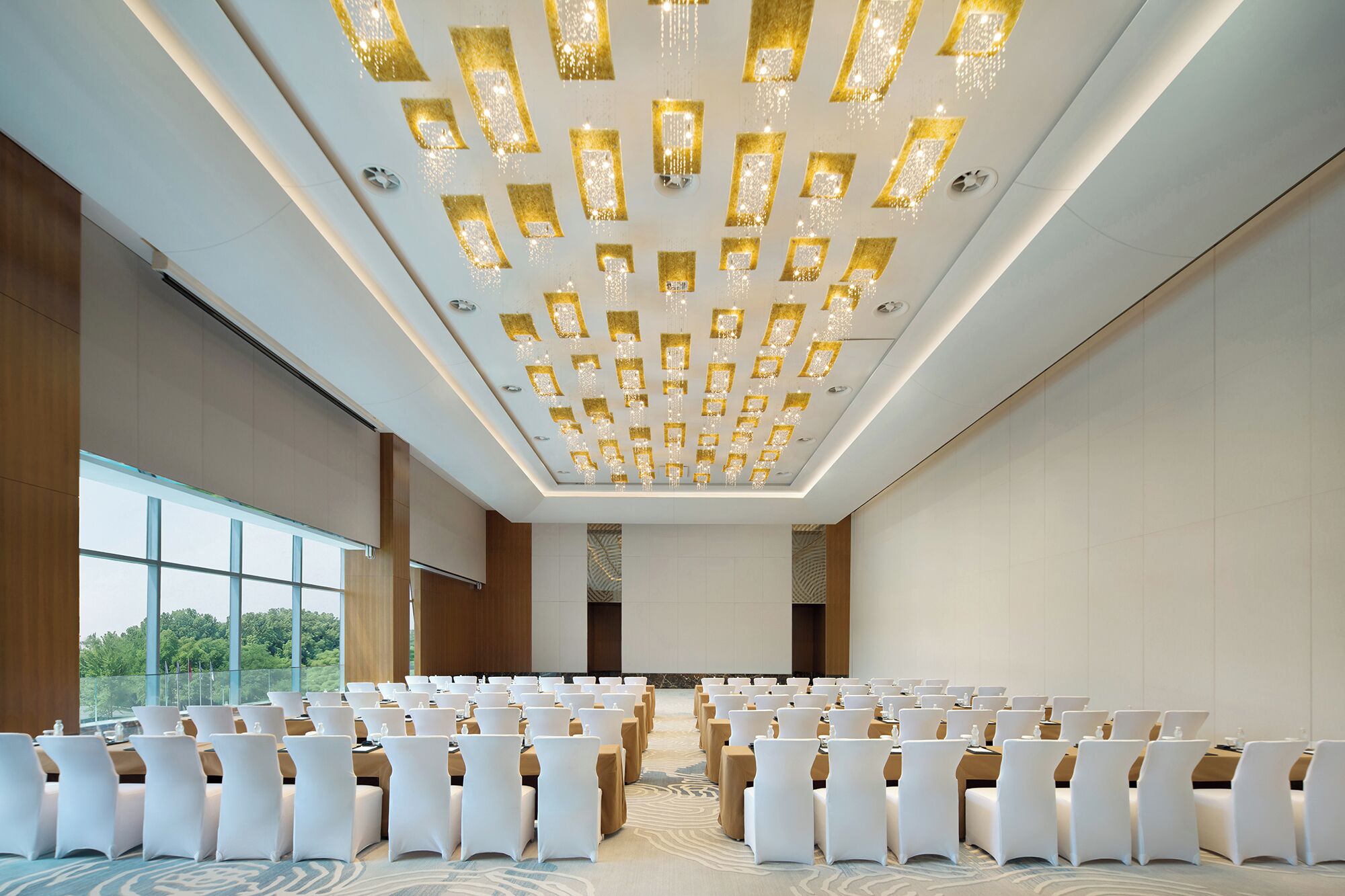 A conference room with rows of white chairs, a patterned carpet, and a ceiling with a unique light fixture.