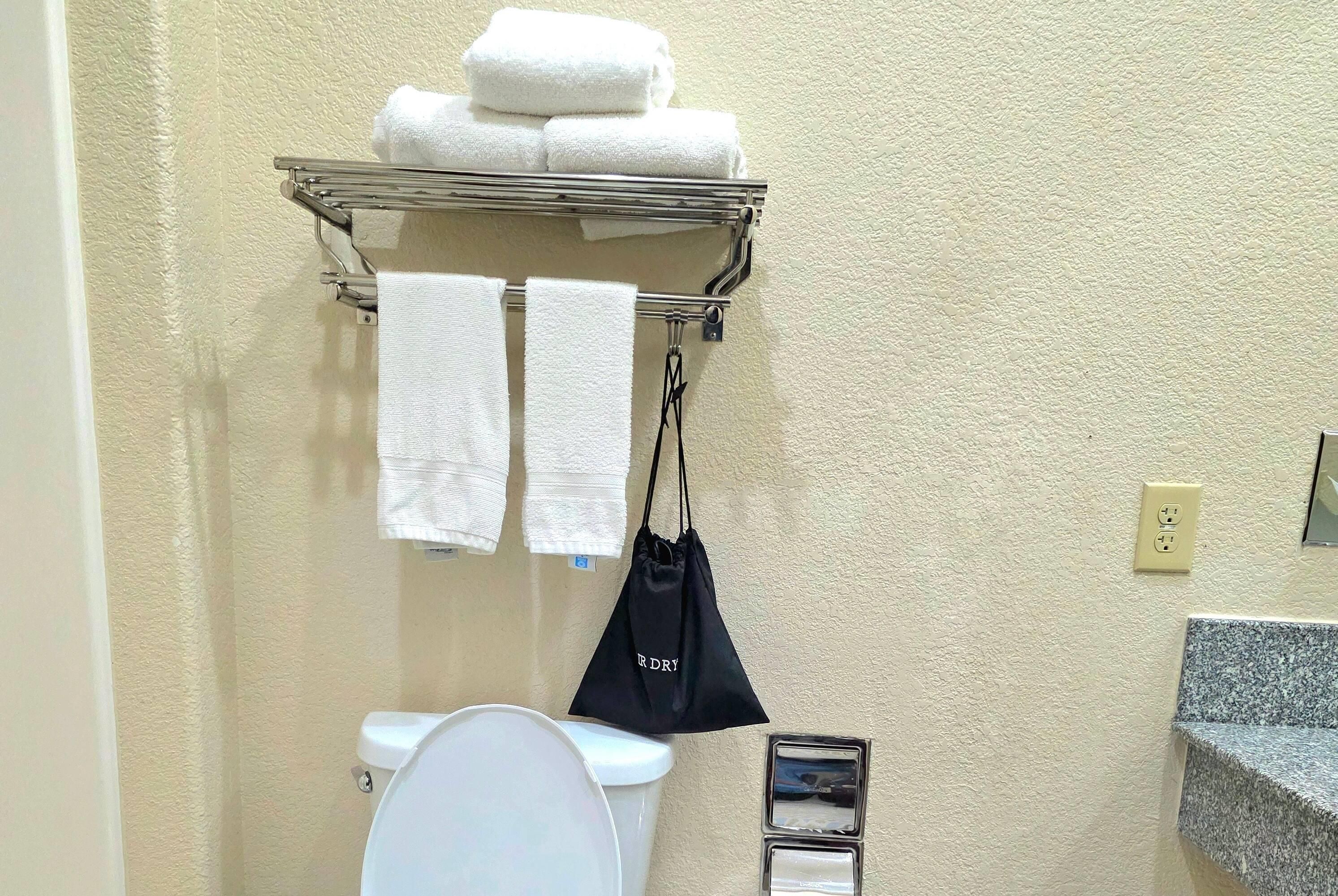 Un baño con inodoro, toallero con toallas, una bolsa negra y encimera de granito.