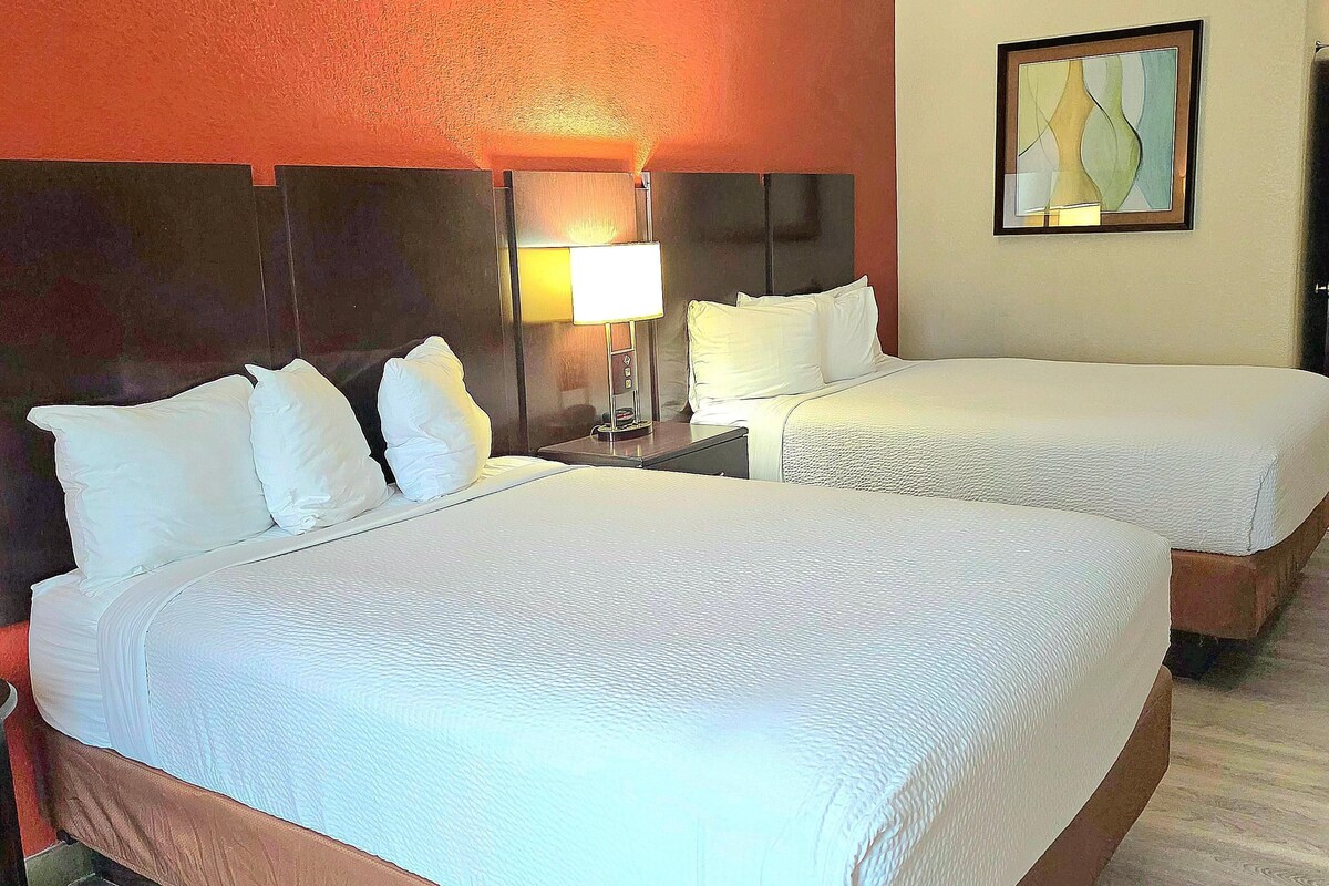 A hotel room with two beds, a nightstand with a lamp, and a painting on the wall.