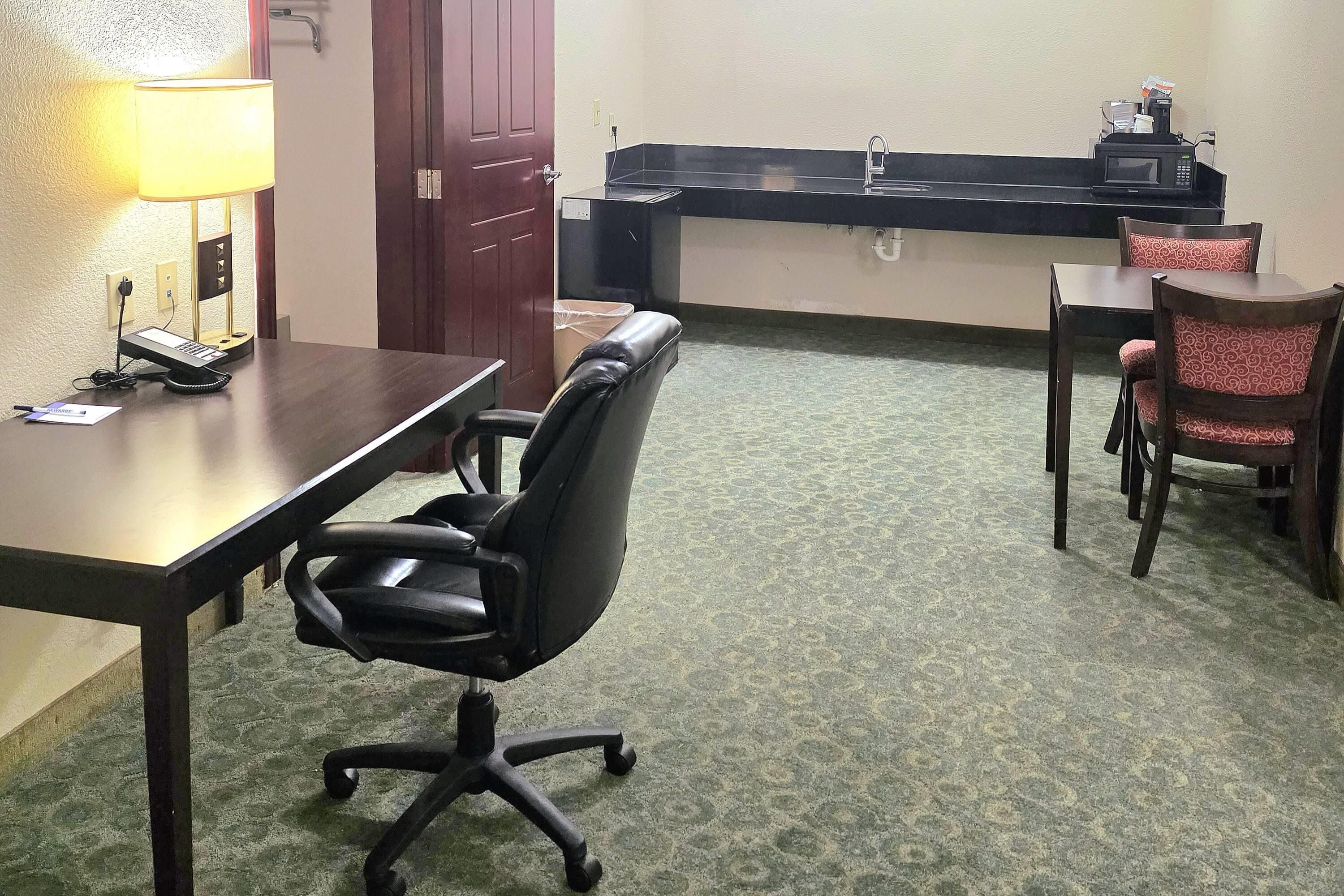 A hotel room with a desk, office chair, a telephone, a lamp, a microwave, and a sink.