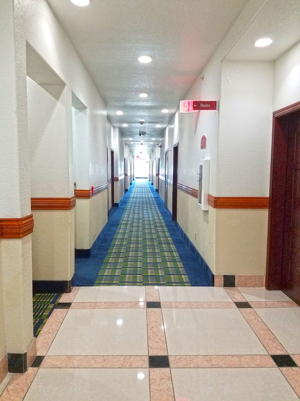 A hotel corridor with a blue carpet, tiled floor, and doors on both sides. - Ramada by Wyndham South Waco (Hewitt)