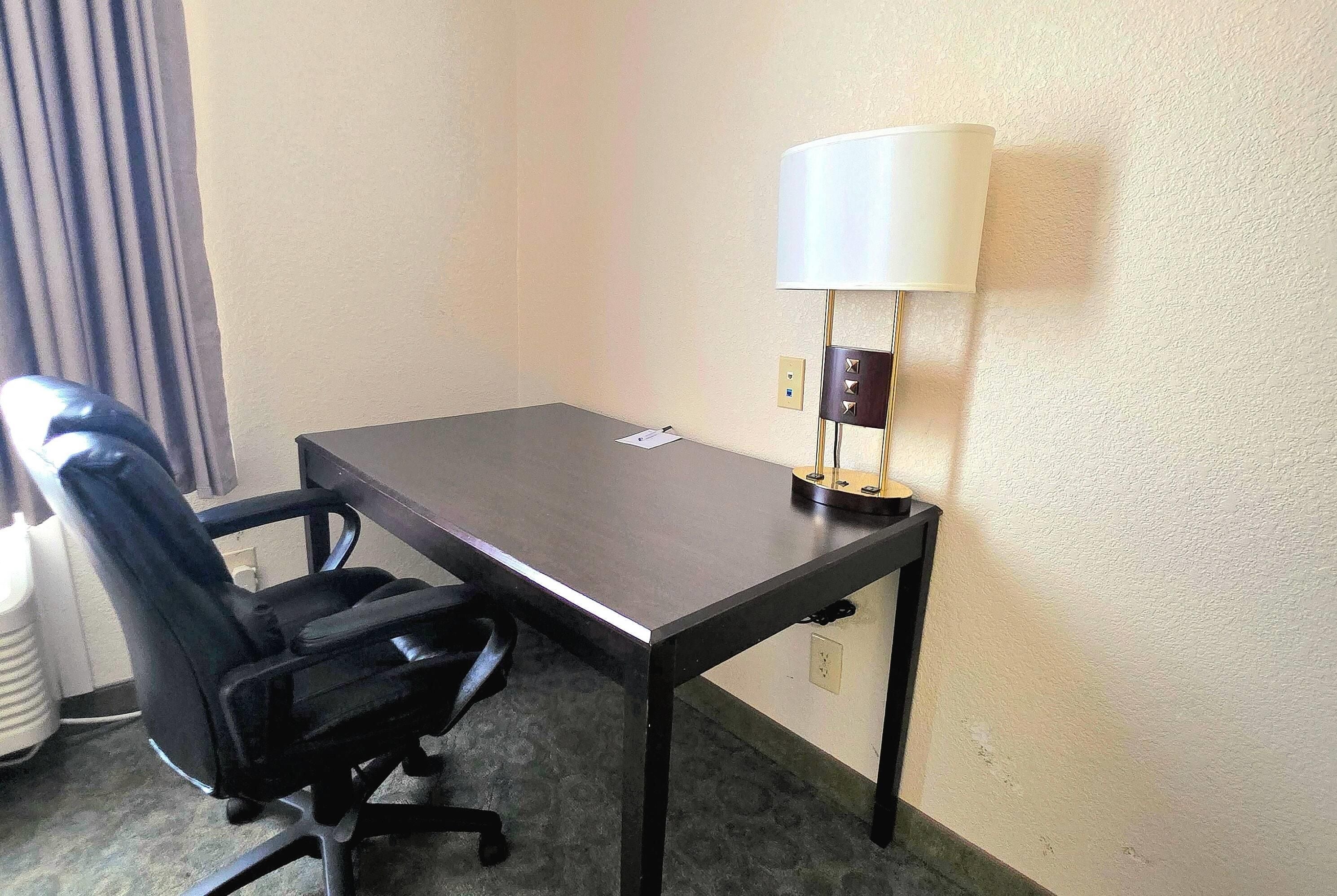 A hotel room with a single desk, a chair, and a lamp.