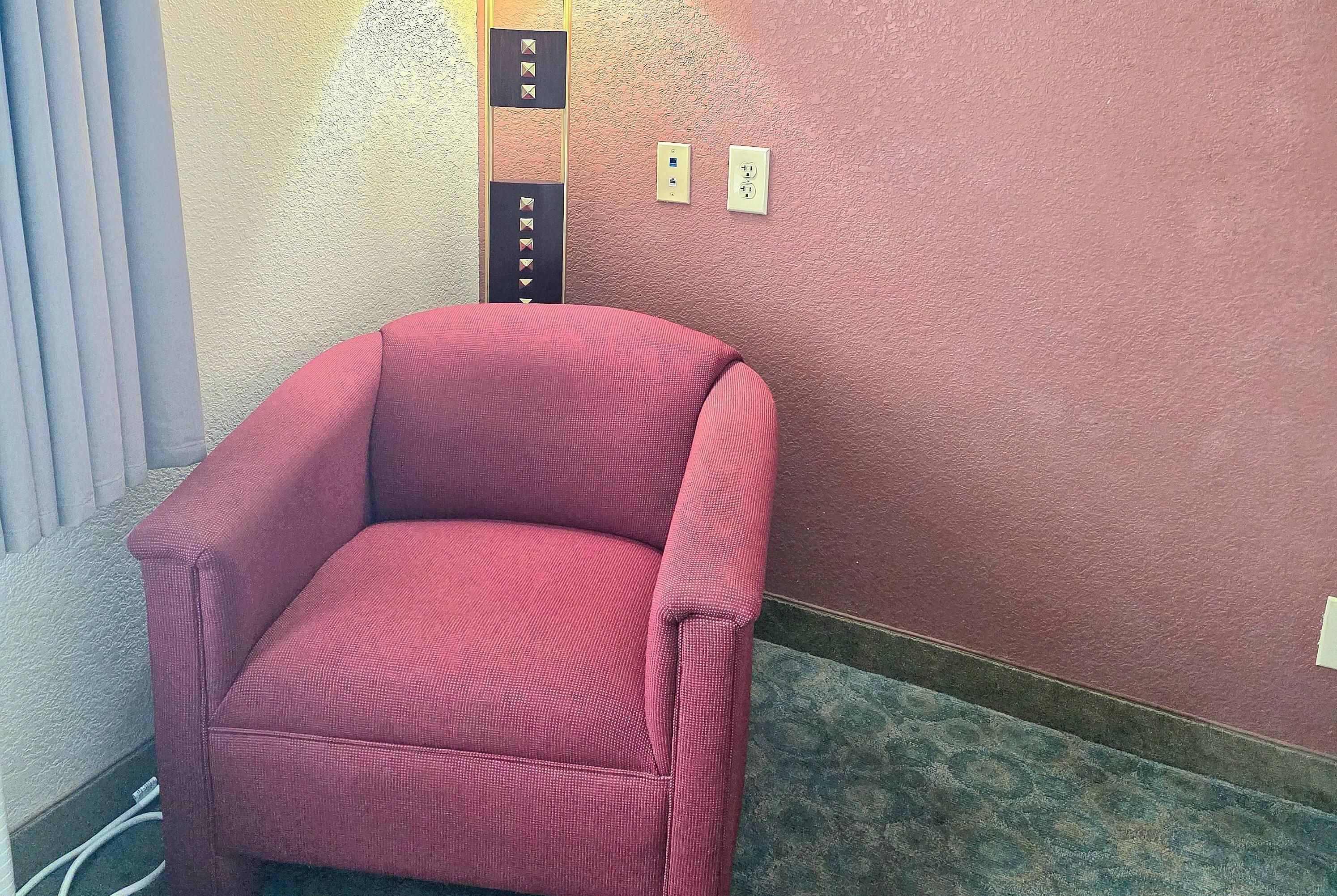Ein roter Sessel steht in einer Ecke des Raumes, dessen Wand eine strukturierte Oberfläche hat und der mit einem Teppich ausgelegt ist.