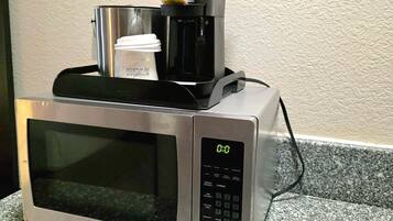 Un microondas con un preparador de café y una taza desechable encima.