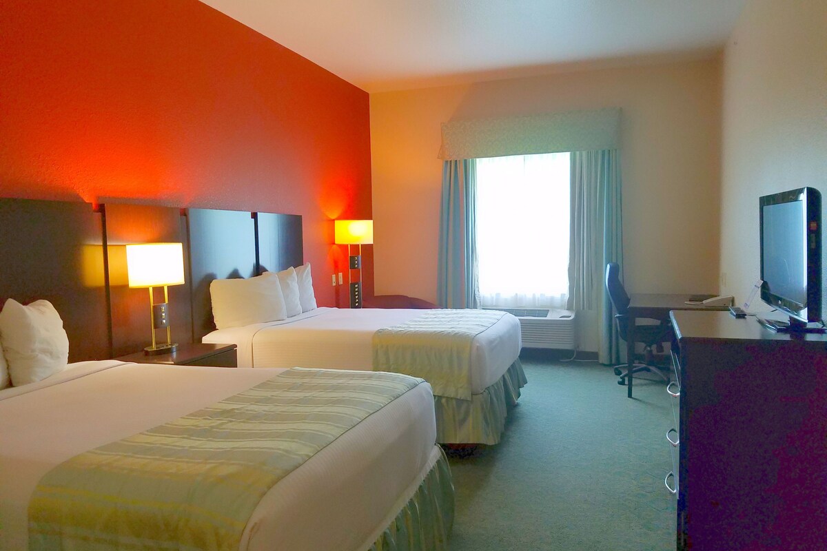 A hotel room with two beds, a desk, a television, and a window with curtains.