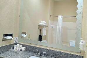 A bathroom with a granite countertop, a towel rack, a shower curtain, and a soap dispenser.