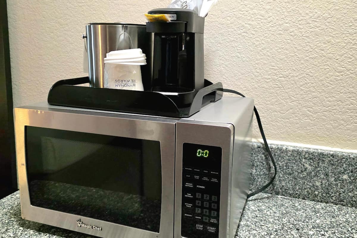 Un microondas con una cafetera encima, un reloj digital y una taza de café.