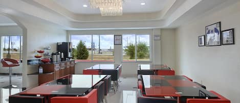 A modern dining area with glass tables and red chairs, large windows with a view of the outside, and a chandelier.