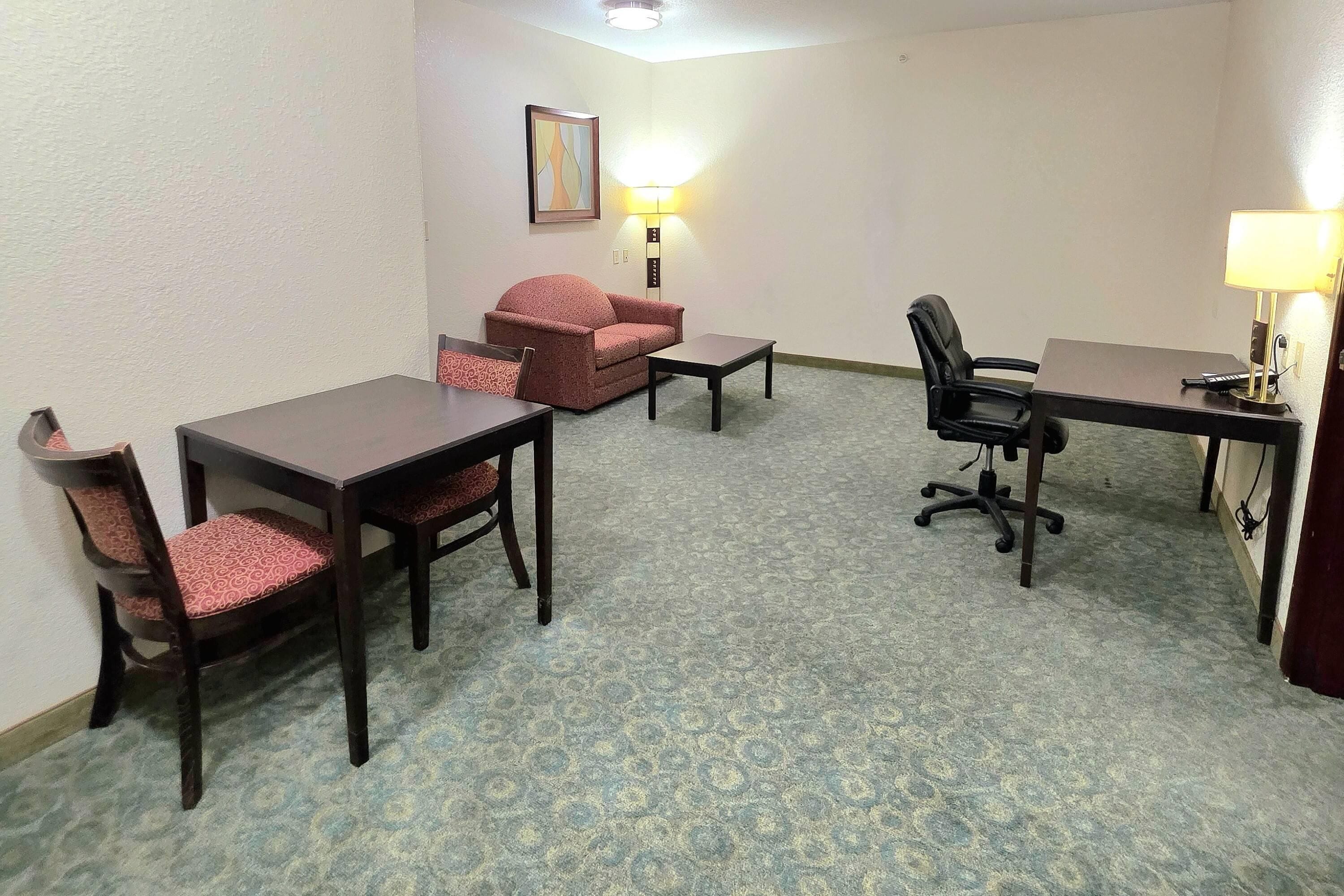 A hotel room with a desk, two chairs, a sofa, and a lamp.