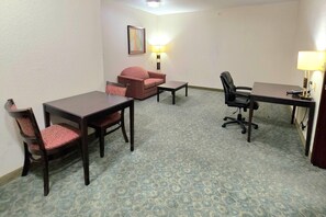 A hotel room with a desk, two chairs, a sofa, and a lamp. - Ramada by Wyndham South Waco (Hewitt)