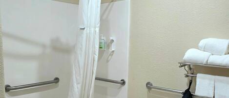 Un baño con cortina de ducha, barras de apoyo, inodoro y toallero con toallas.