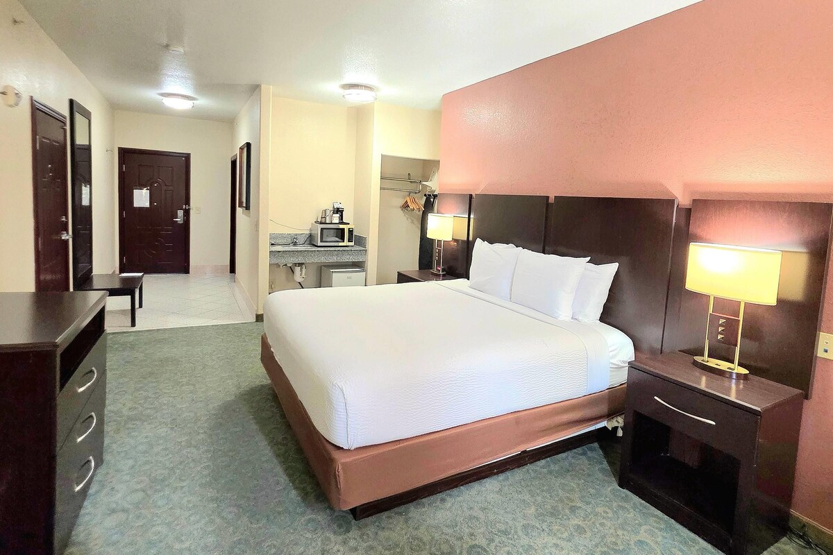 A hotel room with a large bed, a desk, a chair, a microwave, and a lamp.