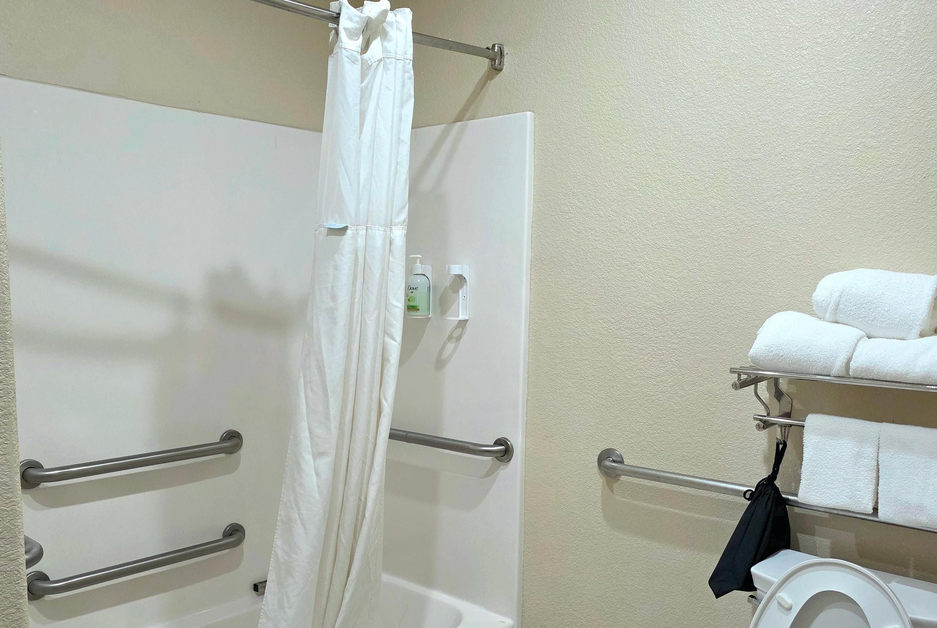 A bathroom with a shower curtain, handrails, a towel rack with towels, and a toilet.