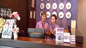 A reception desk with a purple wall, framed pictures, and a vase of flowers.