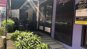Entrada de hotel con área de estar al aire libre techada, plantas en macetas y un cartel.
