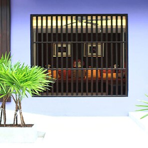 A window with vertical bars, a plant in the foreground, and a glimpse of a room with a bed and a window in the background. - Sawasdee Hotel @ Sukhumvit Soi 8 (Bangkok)