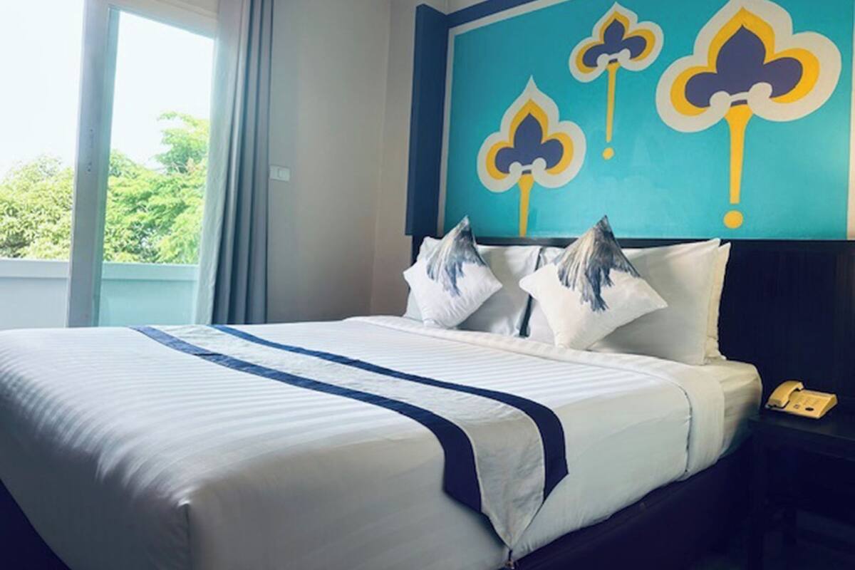 A hotel room with a bed, a nightstand, a telephone, and a window with curtains.