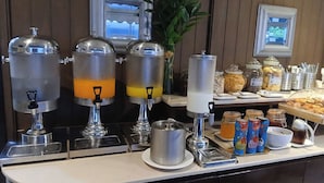 Un bufé de desayuno con múltiples dispensadores de bebidas, una variedad de alimentos y una planta decorativa.