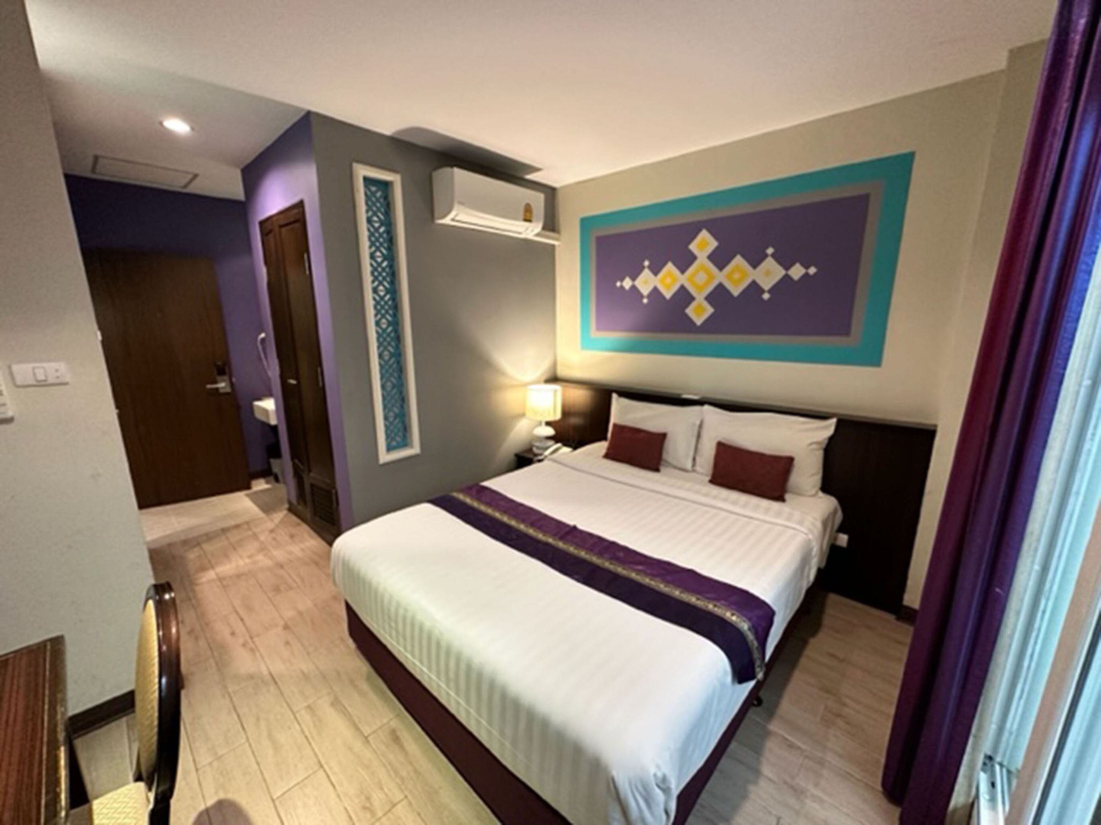 Une chambre d’hôtel comprenant un lit, une table de chevet, un climatiseur fixé au mur et une porte donnant sur une autre pièce.