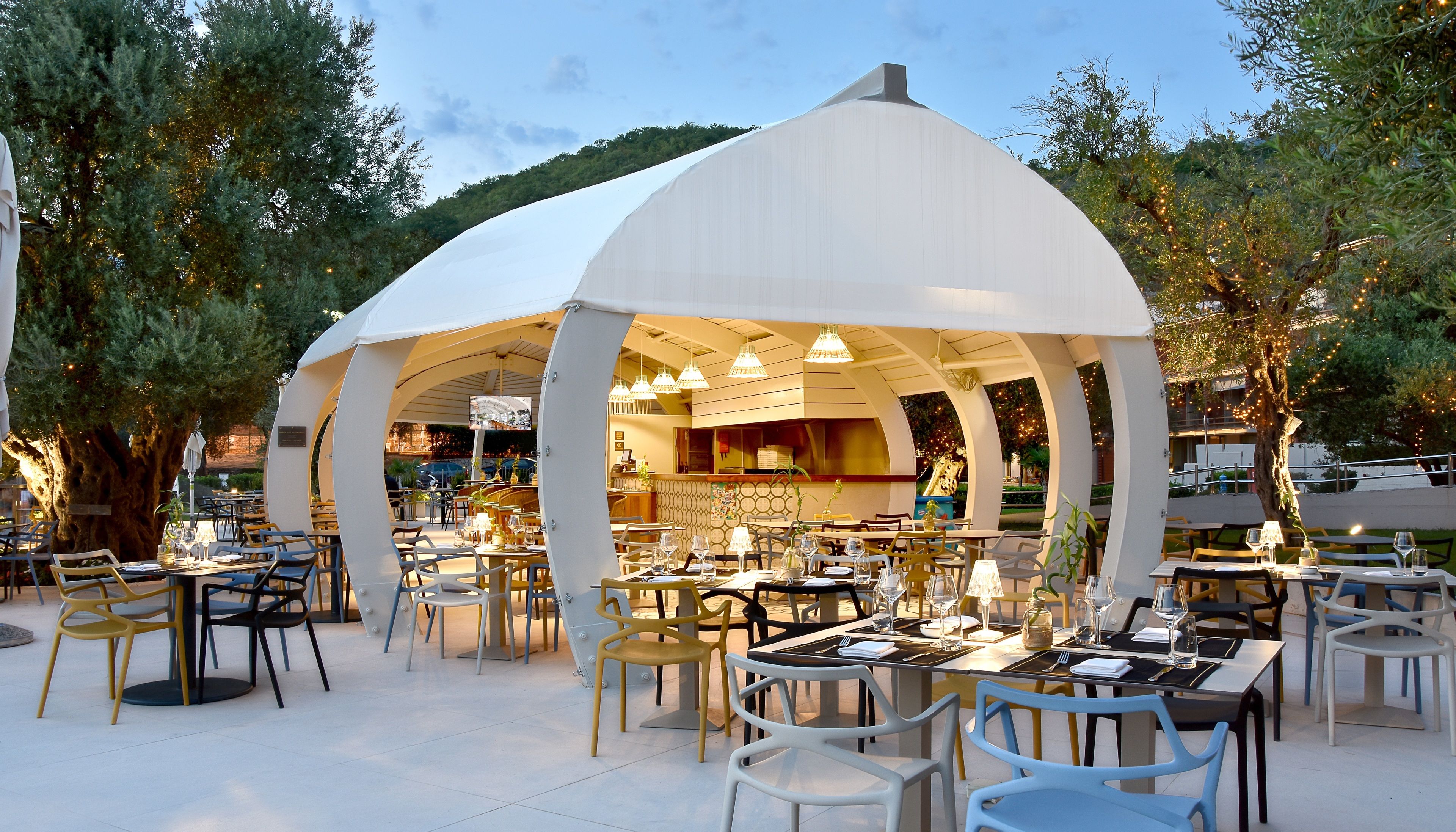 Un área de comedor al aire libre con mesas y sillas, un espacio de estar cubierto y vistas al interior del restaurante.