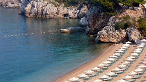 Una playa con agua cristalina, acantilados rocosos y filas de sombrillas y sillas.