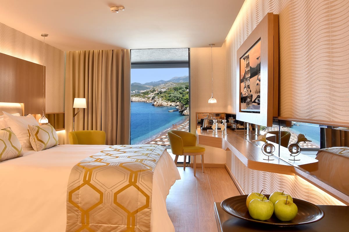 Una habitació d'hotel amb un llit gran, una taula de treball amb vistes i una zona de menjador amb vista al mar.