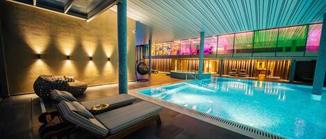 Un área de piscina interior moderna con sillones de descanso, una zona de estar y vistas a la piscina.