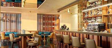 Zona de bar moderna con barra, asientos con taburetes y una variedad de botellas y vasos en estanterías.