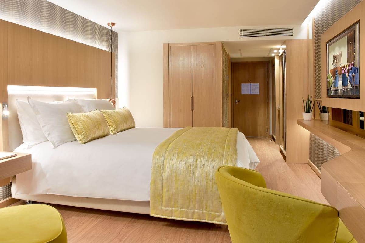 Habitació d'hotel moderna amb un llit gran, una taula de nit amb una làmpada, un escriptori amb una cadira, un televisor i un armari.