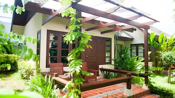 Una casa con porche, sillas de madera y una planta en maceta.